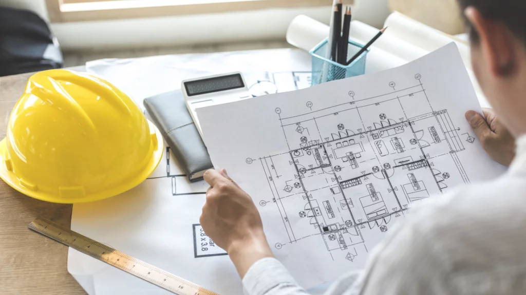 Architect aan het werk met plannetje, helm en rekenmachine op tafel