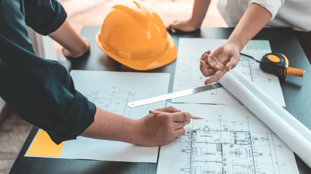 Architect aan het werk met plannetje, helm en rolmaat op tafel